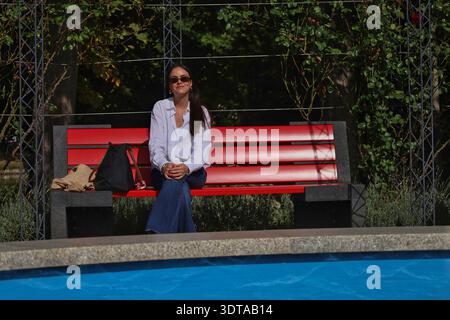 Frau sitzt entspannt auf einer roten Parkbank am Springbrunnen im Sommer, Kurpark Bad Lausick, Landkreis Leipzig, Sachsen, Deutschland Stock Photo