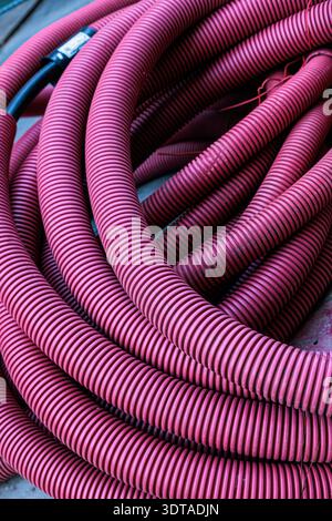 Close-up view of coiled pink corrugated hose highlighting repeating ridged texture and flowing curves; an abstract industrial composition emphasizing Stock Photo