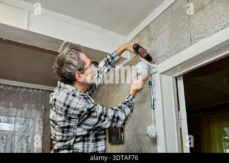 Mature man is installing video surveillance camera inside rural house. Stock Photo