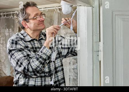After securing surveillance camera bracket above door, farmer connects power. Stock Photo