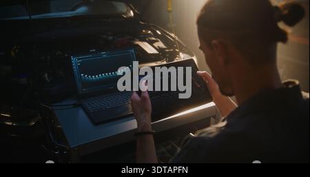 Mechanic With Tablet Analyzing Engine Diagnostics Data. Digital Graphs and Performance Metrics Displayed on Tablet and Laptop Screens. Advanced Automotive Technology, Professional Vehicle Inspection. Stock Photo