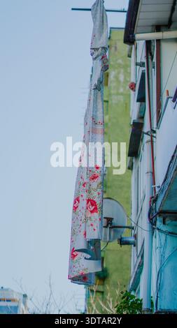 A floral-patterned curtain is draped outside a building in an urban environment under clear skies Stock Photo
