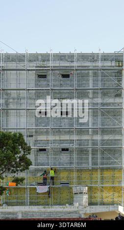 Two construction workers in safety gear work on scaffolding at a building under renovation Stock Photo