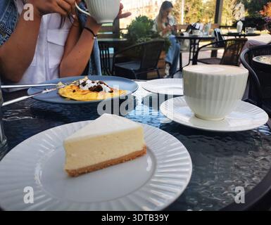 Cheesecake and coffee served at an outdoor café table. This image reflects relaxed dining, social atmosphere and pleasant breakfast moments. Stock Photo