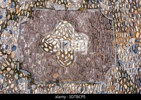 a cobblestone pavement featuring an intricate, symmetrical pattern with alternating dark and light stones forming a geometric design. Stock Photo