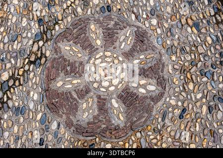 a cobblestone pavement featuring an intricate, symmetrical pattern with alternating dark and light stones forming a geometric design. Stock Photo