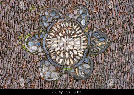 a cobblestone pavement featuring an intricate, symmetrical pattern with alternating dark and light stones forming a geometric design. Stock Photo