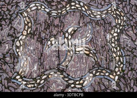 a cobblestone pavement featuring an intricate, symmetrical pattern with alternating dark and light stones forming a geometric design. Stock Photo