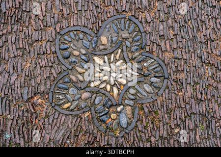 a cobblestone pavement featuring an intricate, symmetrical pattern with alternating dark and light stones forming a geometric design. Stock Photo