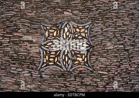 a cobblestone pavement featuring an intricate, symmetrical pattern with alternating dark and light stones forming a geometric design. Stock Photo