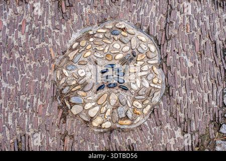 a cobblestone pavement featuring an intricate, symmetrical pattern with alternating dark and light stones forming a geometric design. Stock Photo