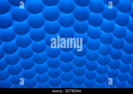 a textured wall featuring a repetitive pattern of evenly spaced, semi-circular, three-dimensional bumps. The bumps are uniformly blue with a slight gr Stock Photo
