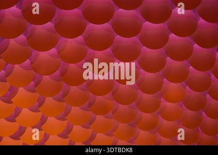 a textured wall featuring a repetitive pattern of evenly spaced, semi-circular, three-dimensional bumps. The bumps are uniformly red with a slight gra Stock Photo
