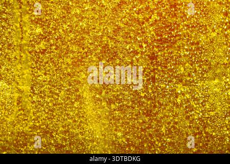 a vibrant golden surface covered in numerous small water droplets. The red background is slightly textured, creating a subtle gradient effect. Stock Photo