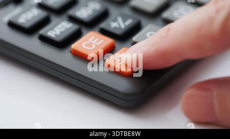 A finger pressing the orange ON button on a black office calculator. Shallow depth of field. Close up. Stock Photo