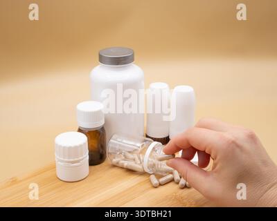 Hand choosing a pill from a spilled bottle of capsules, blending with various medical containers on a wooden surface Stock Photo