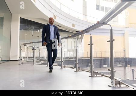 Mature black businessman walking along office balcony with laptop in hand Stock Photo