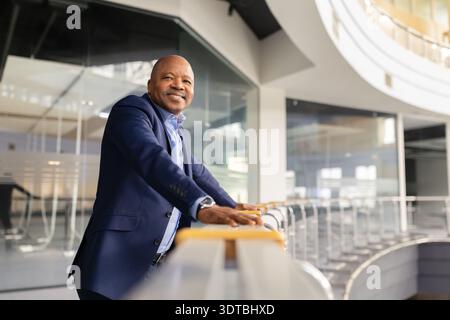 Mature black businessman leaning on balcony railing in office building and smiling Stock Photo