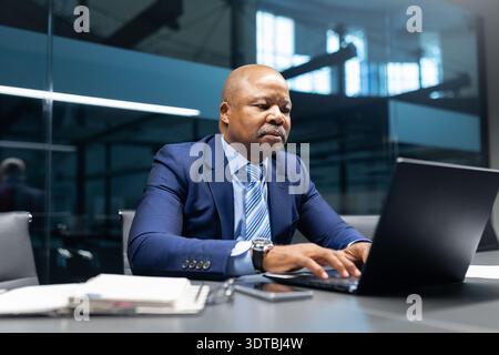 Serious mature black businessman typing on laptop at desk in contemporary office Stock Photo