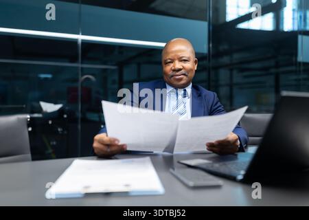 Confident mature black businessman reviewing documents while sitting at desk in office Stock Photo