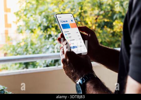 Man at home checking the financial app on his mobile phone. Digital wallet, home finances concepts. Stock Photo