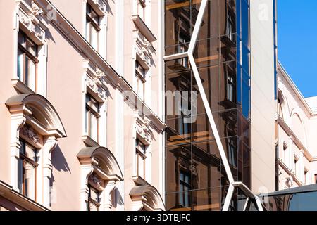 A historic building with decorative elements stands beside a contemporary structure featuring a reflective glass facade, showcasing architectural cont Stock Photo