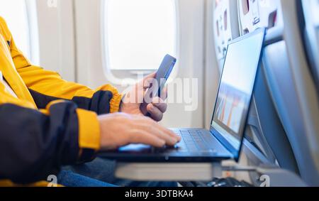 Closeup of adult man working on laptop and holding smartphone during flight Stock Photo