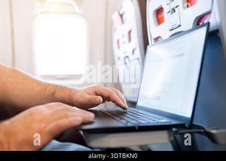 Adult caucasian male traveler working on laptop by airplane window Stock Photo