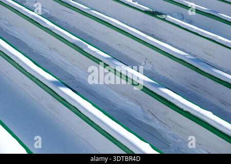 Bright sunlight glimmers on freshly fallen snow atop green benches in a park. Stock Photo