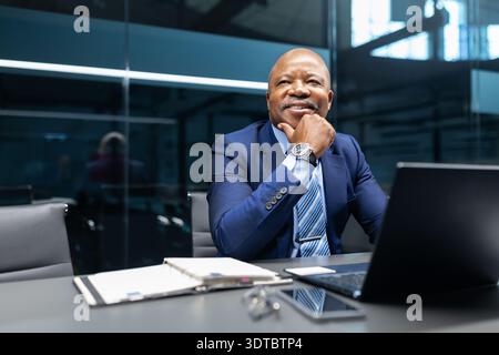 Thoughtful mature black businessman looking away while sitting at desk in office Stock Photo