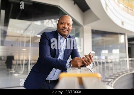 Mature black businessman using smartphone while leaning on office railing Stock Photo