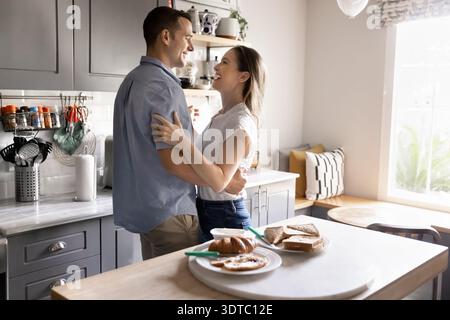 Couple embracing and laughing during romantic morning in kitchen Stock Photo