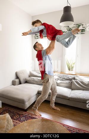 Father and son wearing red superhero capes playing indoor Stock Photo