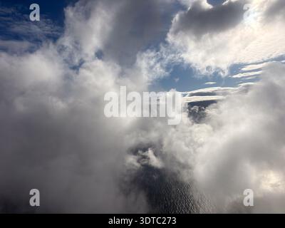 Thick, dramatic clouds viewed from above the ocean or sea. Aerial view through breaks in the cumulus and stratus, showing deep blue sky and water belo Stock Photo