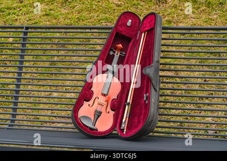 Violin and bow in a red case on a bench in the park Stock Photo