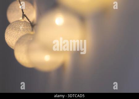 White cotton ball string lights hanging in a cluster with soft warm illumination and strong bokeh blur for cozy hygge home interior design and minimal Stock Photo