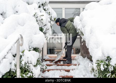 man 55 years old removes snow with shovel in winter on stairs at house entrance after snowfall. Stock Photo