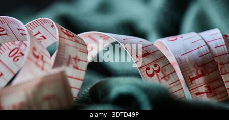 Close up of a white and red measuring tape resting on dark green textile material Stock Photo