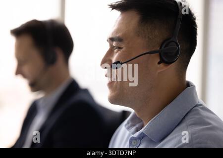 Smiling young man hotline operator in headphones receiving phone call Stock Photo