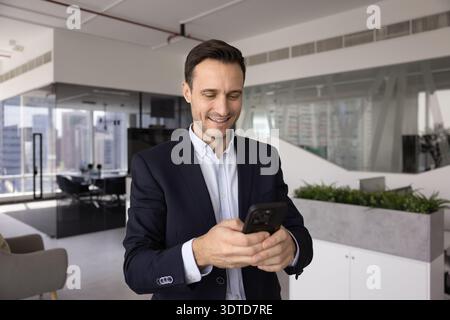 Smiling adult businessman working on mobile phone in company office Stock Photo