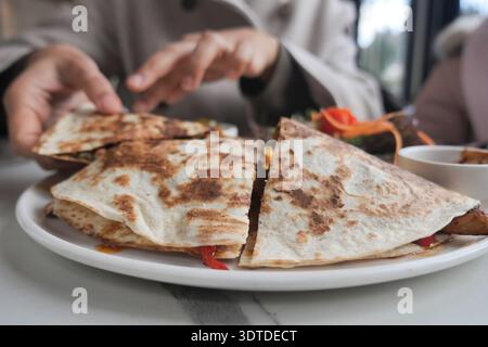 Hands reach for quesadilla on a white plate in a restaurant Stock Photo