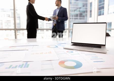 Laptop screen with white mockup, statistical data displaying in papers Stock Photo