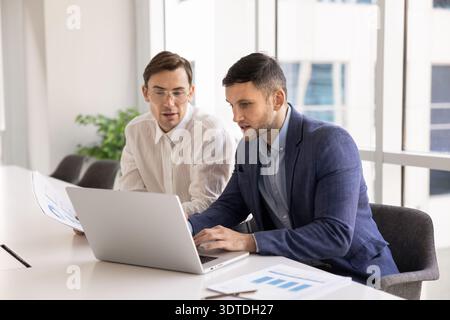 Two focused young businessmen sitting at conference desk using laptop Stock Photo