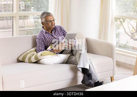 Focused old man dressed casually wear glasses using digital tablet Stock Photo