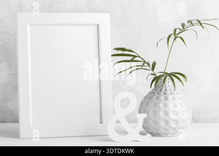 Small modern vase with branch of palm leaves and empty frame mock up on the shelf, grey stone wall room minimalistic interior design Stock Photo