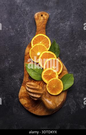 Slices of ripe orange on olive wood cutting board over black slate background.Top view with copy space Stock Photo