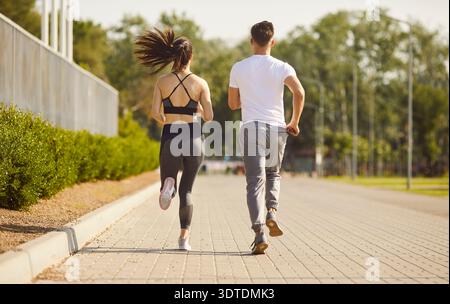 Couple running together on path under sunlight, outdoor exercise, moving for health and fitness Stock Photo