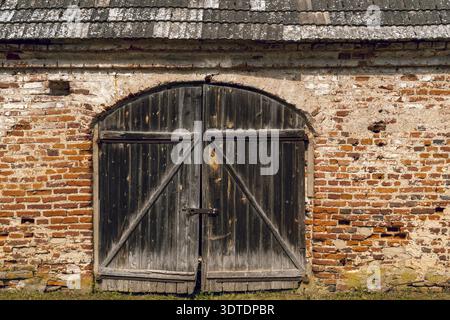 Wooden gate of old building made by red bricks. Entrance to medieval old castle. Ancient red brick wall with a wooden doors Stock Photo