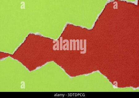 Hole ripped in a green paper on red background. Copy space Stock Photo
