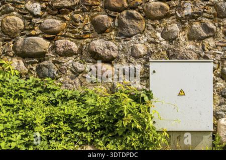 Metal electrical control cabinet against a rough stone wall Stock Photo